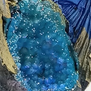 K&ouml;nnte beinhalten: Eine blaue und goldene Drachenfigur mit einem kristallartigen blauen Edelstein, der in seinen R&uuml;cken eingebettet ist. Der Drache sitzt auf einem felsigen Sockel.