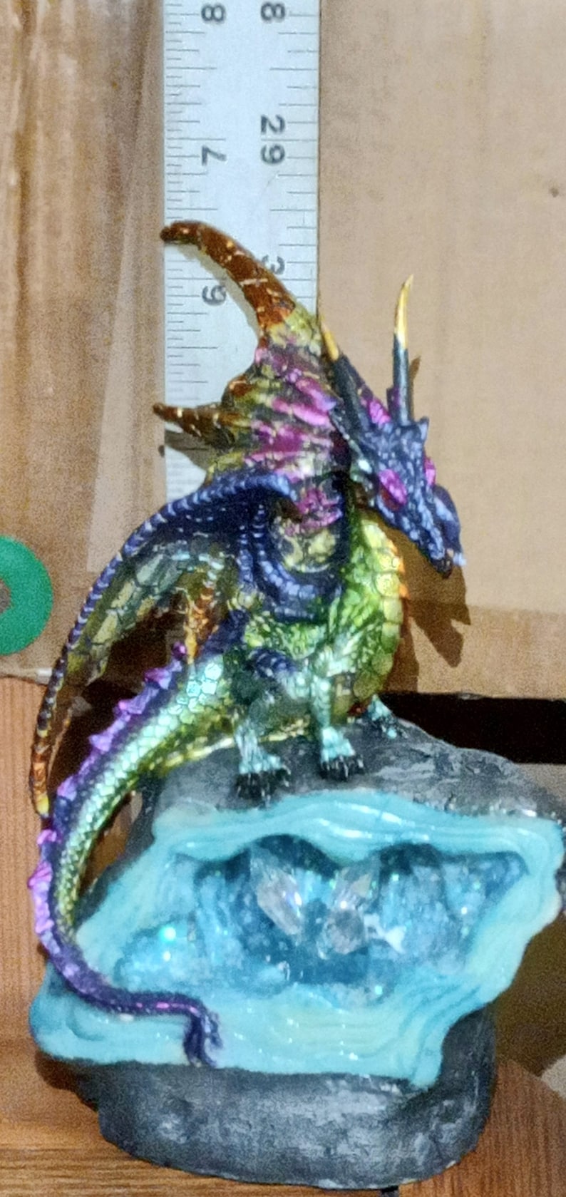 May include: A multi-colored dragon figurine with iridescent scales, perched on a blue and gray rock base with a crystal-like texture. The dragon has a long tail and a horn on its head.