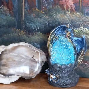 K&ouml;nnte beinhalten: Eine blaue Drachenfigur mit goldenen Akzenten, die sich um einen gro&szlig;en blauen Kristall schlingt. Der Drache sitzt auf einem schwarzen Felssockel.