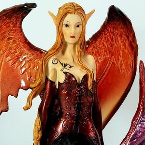 May include: A fantasy figurine of a female with pointed ears, long flowing red hair, and large wings. She is wearing a red and black corset and a long black skirt. The wings are a mix of orange and red.