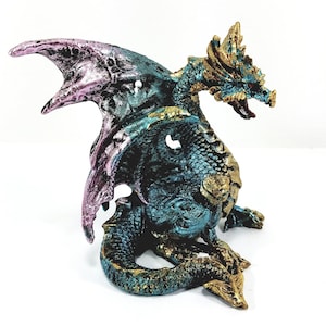 May include: A teal and gold dragon figurine with pink wings. The dragon is sitting on its haunches with its wings spread out.