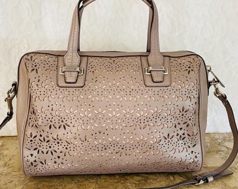 May include: A beige leather handbag with a floral cut-out design. The bag has two handles and a detachable shoulder strap. The Coach logo is visible on the front. The bag is approximately 12 inches wide and 8 inches tall.
