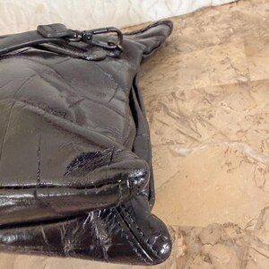 May include: A black quilted leather handbag with a zipper closure and a silver-tone clasp. The bag has a glossy finish and a structured shape. The stitching creates a diamond pattern across the surface of the bag.