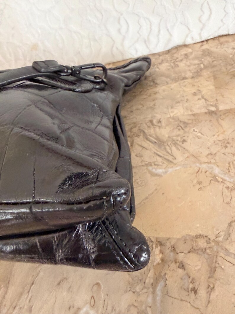 May include: A black quilted leather handbag with a zipper closure and a silver-tone clasp. The bag has a glossy finish and a structured shape. The stitching creates a diamond pattern across the surface of the bag.