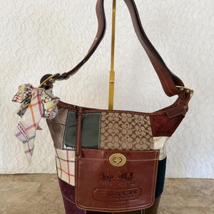 May include: A patchwork Coach handbag with a brown leather strap and a small front pocket. The bag features a variety of textures and colors, including brown, green, and burgundy. A patterned scarf is tied to the handle.