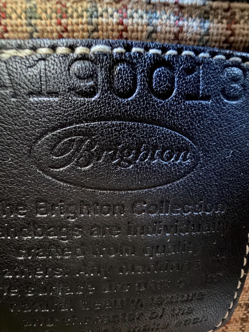 Op de afbeelding: Een zwarte leren patch met witte stiksels voorzien van de in reli&euml;f aangebrachte tekst Brighton en het nummer 190018. De tekst luidt: The Brighton Collection handbags are individually crafted from quality leathers. Any markings on the surface are part of its natural beauty, texture, and character of the leather.