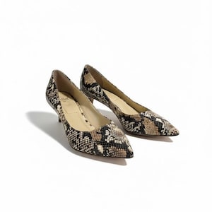 May include: A pair of snakeskin-patterned court shoes in brown, black, and beige. The shoes have a low heel and a pointed toe. They are set against a white background.