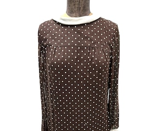 Puede incluir: Un vestido marrón con lunares blancos y un cuello blanco. El vestido tiene mangas largas y una silueta ajustada.