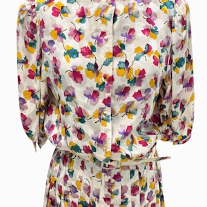 May include: A white dress with a floral print in shades of pink, yellow, green, and purple. The dress has a button-up front and a pleated skirt.