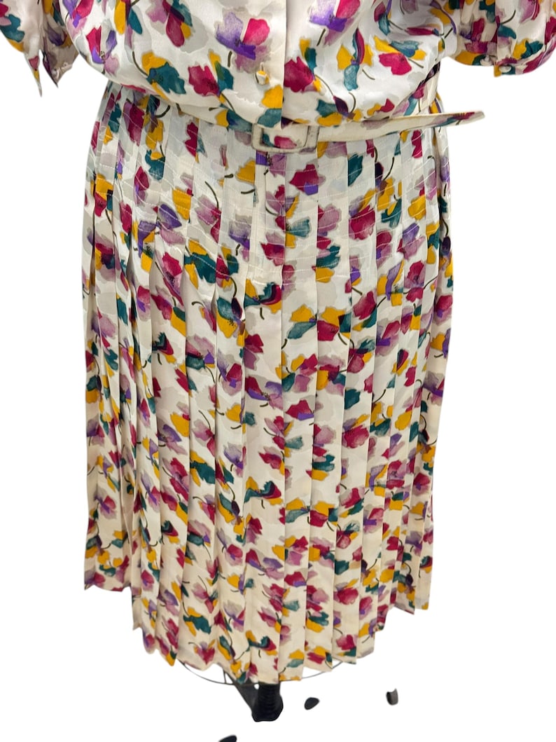 May include: A white pleated skirt with a floral print in shades of pink, purple, yellow, and green.