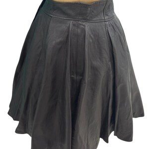 May include: A black leather skirt with a pleated design. The skirt is knee-length and has a high waist.