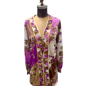 May include: A long-sleeved, open-front garment with a floral pattern in shades of purple, brown, and white. The garment has a cream-colored trim and is displayed on a mannequin. The floral design is a prominent feature.