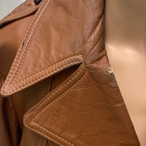 Peut inclure: Une veste en cuir marron avec un col qui se rabat. La veste a une fermeture &agrave; bouton et un d&eacute;tail de couture autour du col.