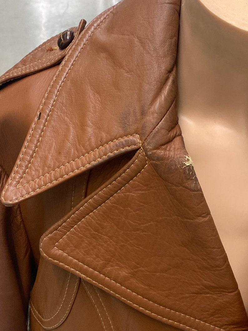 Peut inclure: Une veste en cuir marron avec un col qui se rabat. La veste a une fermeture &agrave; bouton et un d&eacute;tail de couture autour du col.