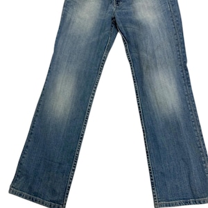 May include: Faded blue denim jeans with a classic five-pocket design. The jeans have a mid-rise waist and a slight bootcut leg opening. The denim has a worn appearance with subtle fading and whiskering details.