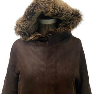 May include: A brown leather jacket with a fur-lined hood. The jacket has a long sleeve and a relaxed fit.
