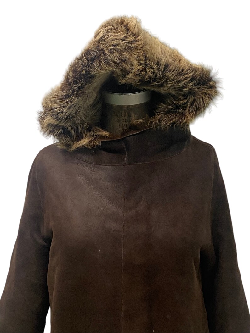 May include: A brown leather jacket with a fur-lined hood. The jacket has a long sleeve and a relaxed fit.