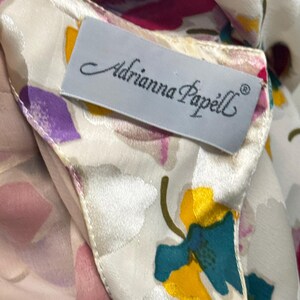 May include: A white silk scarf with a floral print. The scarf has a label that reads "Adrianna Papell".