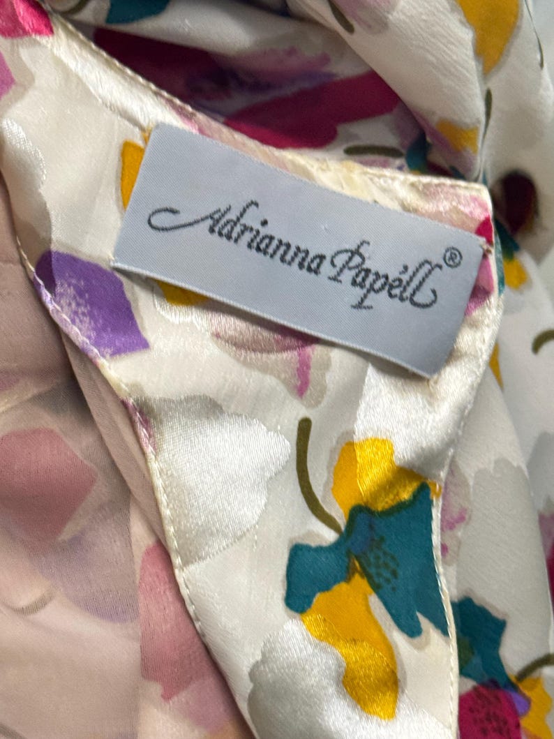 May include: A white silk scarf with a floral print. The scarf has a label that reads "Adrianna Papell".
