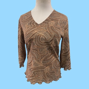 Op de afbeelding: Een bruin en gouden longsleeve shirt met een draaiend patroon. Het shirt heeft een v-hals en een gerimpelde zoom.