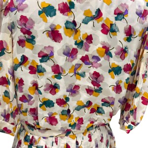 May include: A white dress with a floral print featuring pink, purple, yellow, and green flowers. The dress has a pleated skirt and short sleeves.