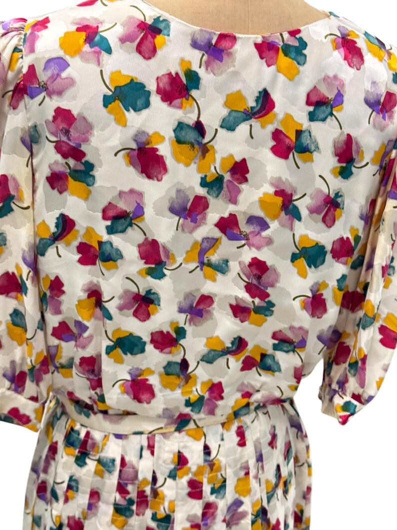 May include: A white dress with a floral print featuring pink, purple, yellow, and green flowers. The dress has a pleated skirt and short sleeves.