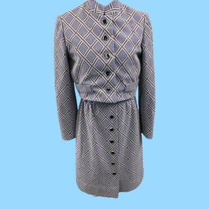May include: A two-piece dress set with a skirt and a matching jacket. The fabric is a white and black geometric pattern with a blue accent. The dress has a button-up front.