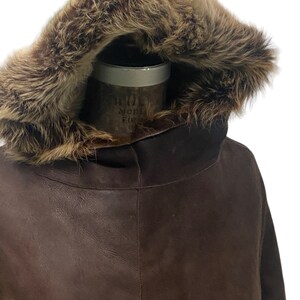 May include: A brown leather jacket with a fur-lined hood. The hood is up and the fur is visible.
