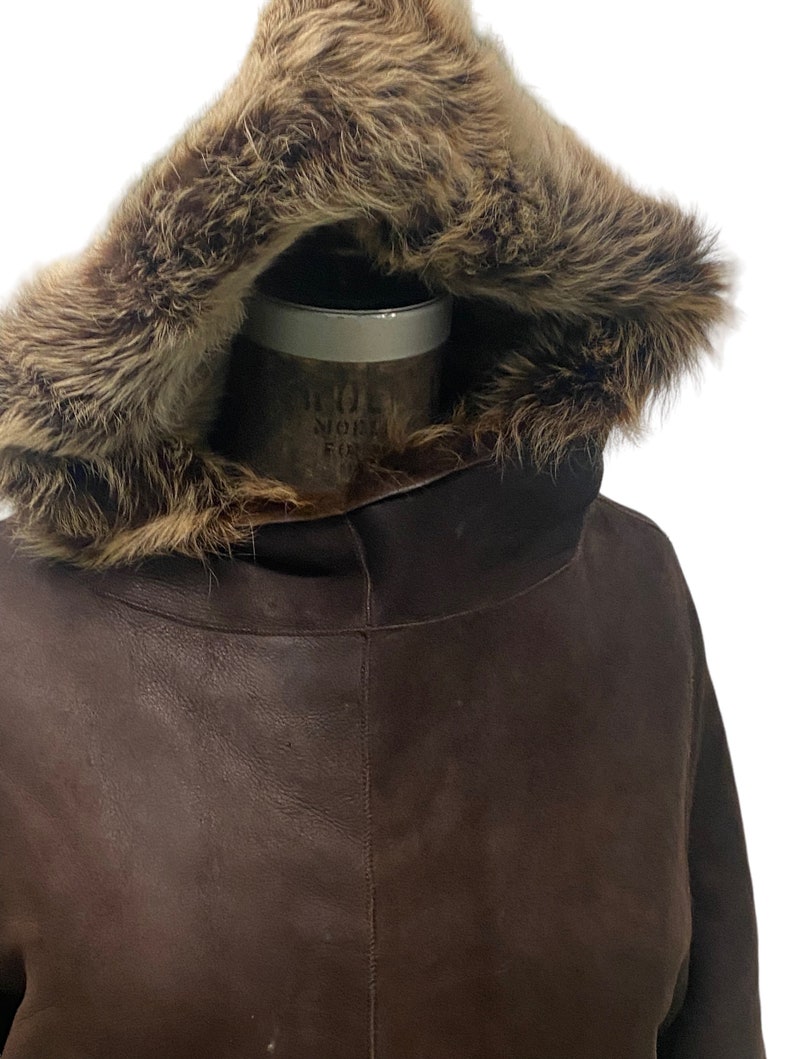 May include: A brown leather jacket with a fur-lined hood. The hood is up and the fur is visible.