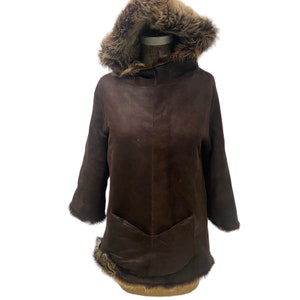 May include: A brown suede hooded jacket with a fur trim around the hood and the bottom hem. The jacket has a single pocket on the front.