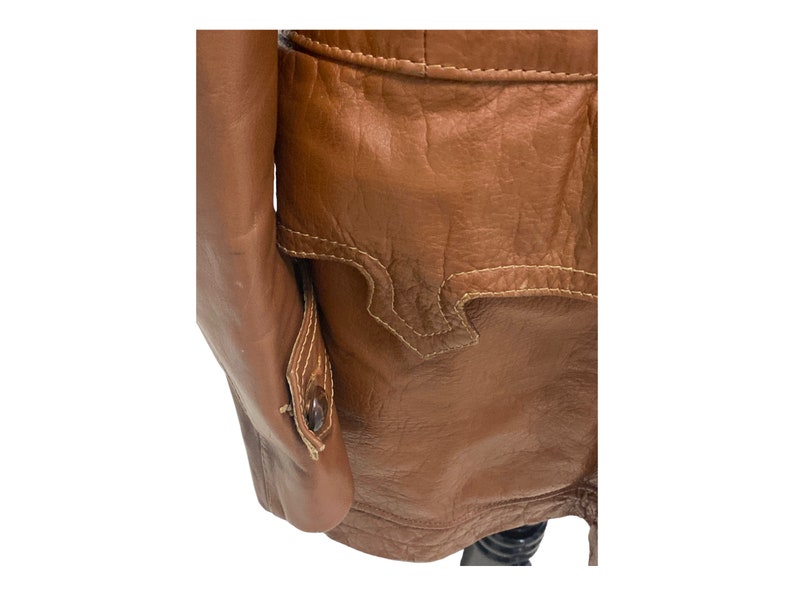 Peut inclure: Une veste en cuir marron avec un bouton sur la manche et un d&eacute;tail de couture d&eacute;coratif au dos.