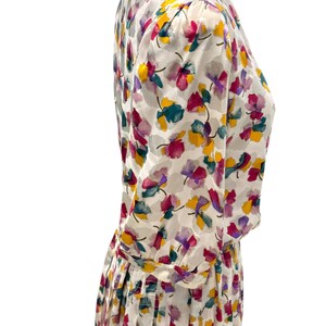 May include: A white dress with a floral print in shades of pink, purple, yellow, and green. The dress has a gathered skirt and long sleeves.
