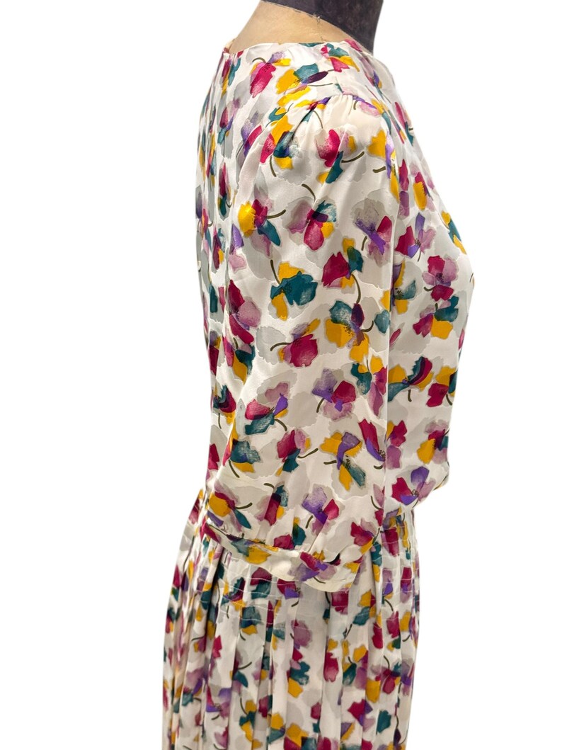May include: A white dress with a floral print in shades of pink, purple, yellow, and green. The dress has a gathered skirt and long sleeves.
