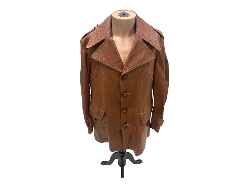 Peut inclure: Une veste en cuir marron avec un col et quatre boutons. La veste a deux poches sur le devant et une ceinture &agrave; la taille.