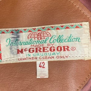Peut inclure: Une veste en cuir marron avec une &eacute;tiquette blanche qui indique "International Collection Made by McGregor" et "Leather Clean Only". L'&eacute;tiquette comporte &eacute;galement une &eacute;tiquette de taille indiquant "42".