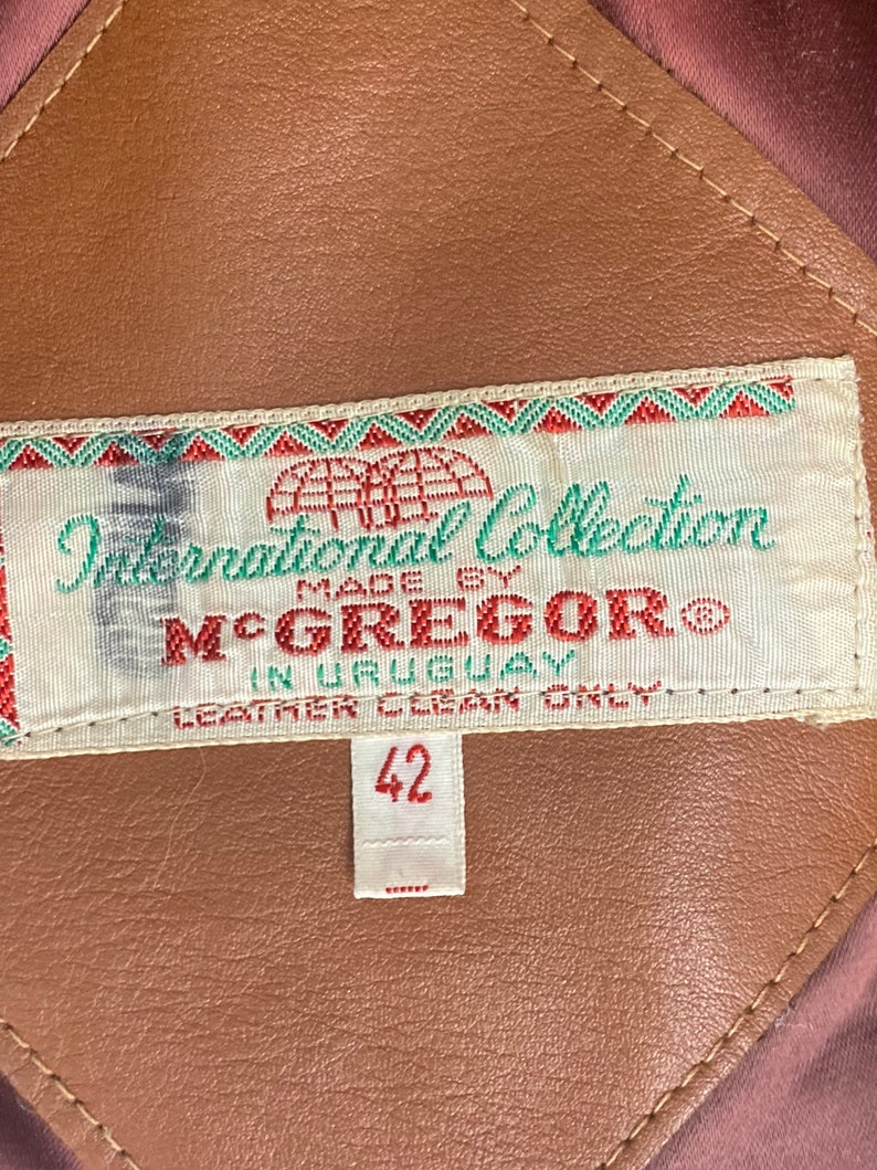 Peut inclure: Une veste en cuir marron avec une &eacute;tiquette blanche qui indique "International Collection Made by McGregor" et "Leather Clean Only". L'&eacute;tiquette comporte &eacute;galement une &eacute;tiquette de taille indiquant "42".