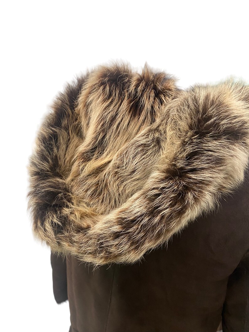 May include: A brown suede jacket with a large, fluffy fur hood. The fur is a mix of brown and beige.