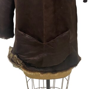 May include: A brown suede jacket with a fur trim around the collar and hem. The jacket has a single patch pocket on the back.