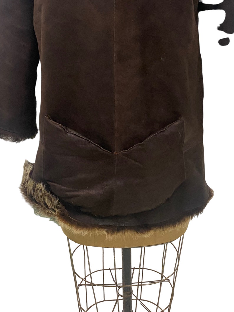 May include: A brown suede jacket with a fur trim around the collar and hem. The jacket has a single patch pocket on the back.