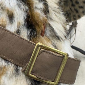 May include: A brown leather belt with a gold metal buckle. The belt is attached to a faux fur garment with a leopard print pattern.