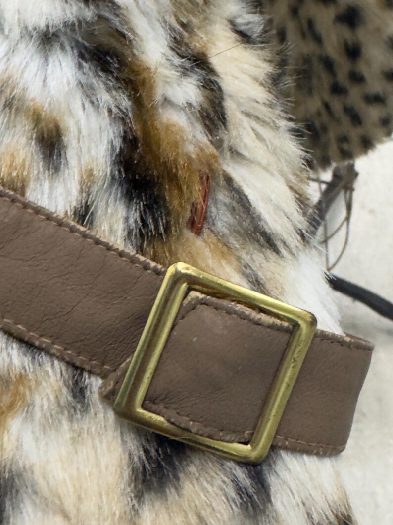 May include: A brown leather belt with a gold metal buckle. The belt is attached to a faux fur garment with a leopard print pattern.