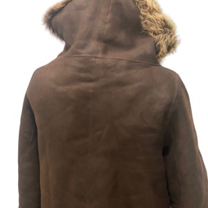 May include: A brown suede jacket with a fur-lined hood. The jacket has a long, fitted style and is perfect for cold weather.