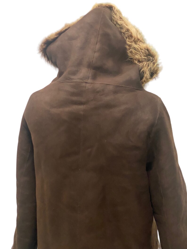May include: A brown suede jacket with a fur-lined hood. The jacket has a long, fitted style and is perfect for cold weather.