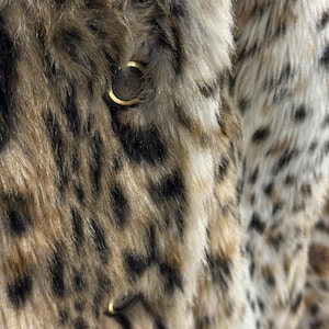 May include: Close-up of a brown and black faux fur jacket with a gold button. The fur has a leopard print pattern.