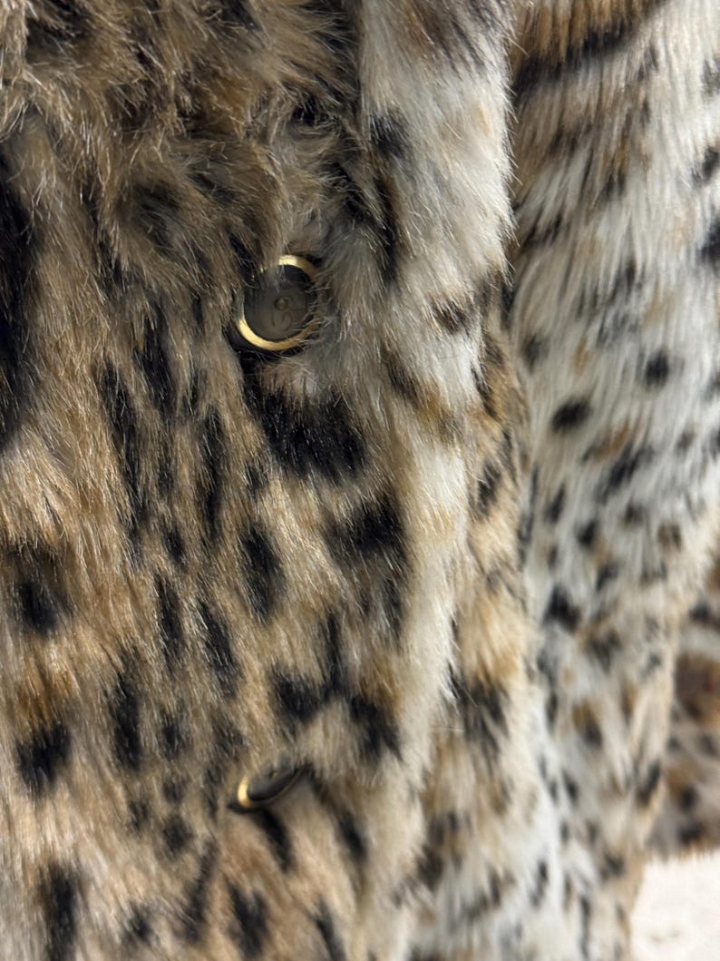 May include: Close-up of a brown and black faux fur jacket with a gold button. The fur has a leopard print pattern.
