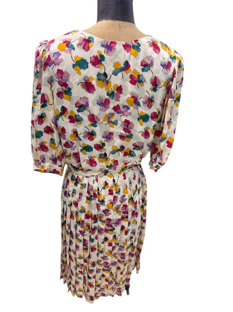 May include: A white dress with a floral print in shades of pink, yellow, green, and purple. The dress has a pleated skirt and a fitted bodice.