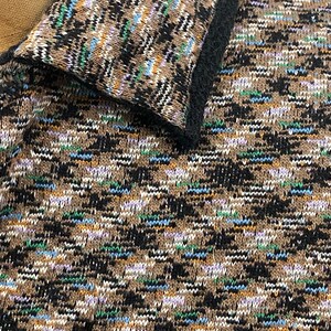 以下が含まれることがあります： 柄物のニットトップのクローズアップ。生地は、茶色、黒、白の織り模様で、青、緑、紫のアクセントがあります。襟は黒いトリムで縁取られています。