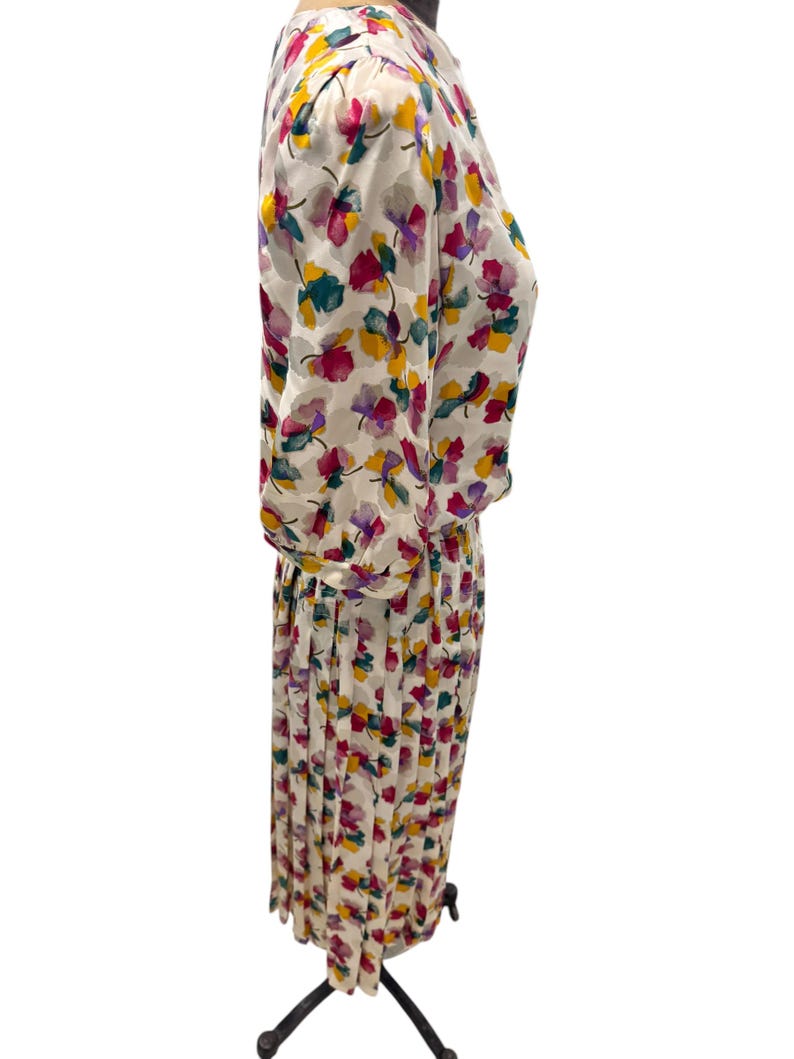 May include: A white dress with a floral print in shades of pink, yellow, green, and purple. The dress has a pleated skirt and a fitted bodice.