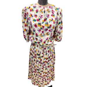 May include: A white dress with a floral print in shades of pink, yellow, green, and purple. The dress has a fitted bodice and a pleated skirt.