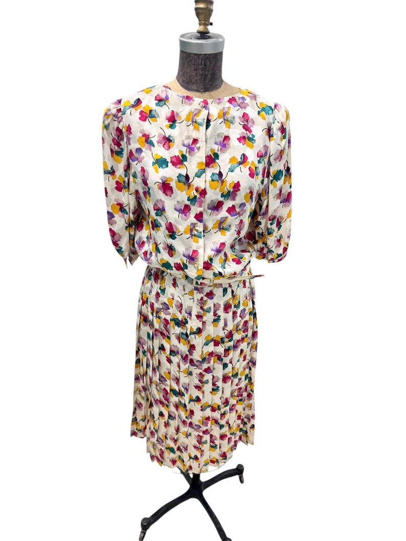 May include: A white dress with a floral print in shades of pink, yellow, green, and purple. The dress has a fitted bodice and a pleated skirt.